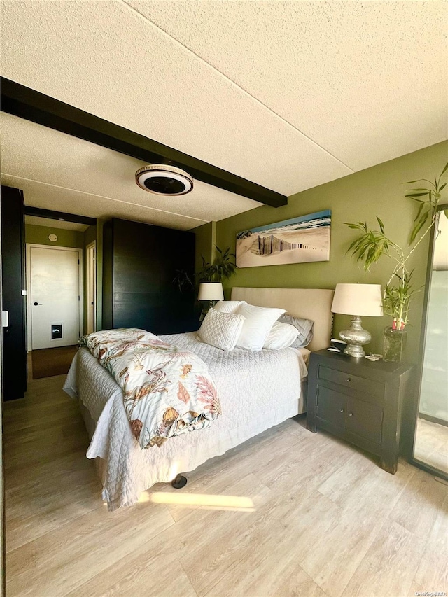 bedroom featuring beam ceiling, hardwood / wood-style floors, and a textured ceiling