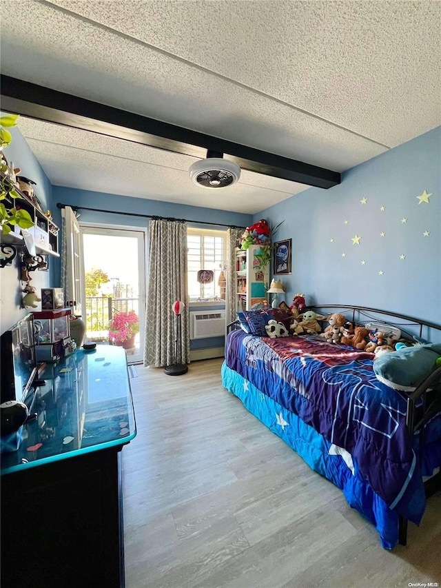 bedroom with beamed ceiling, a textured ceiling, hardwood / wood-style flooring, and an AC wall unit