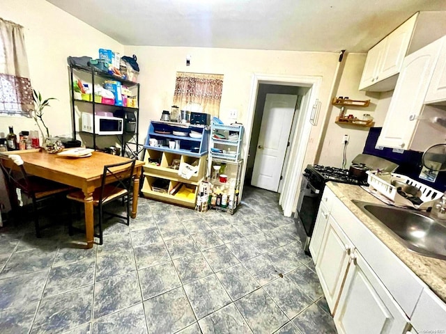 kitchen with gas range oven, white cabinets, and sink