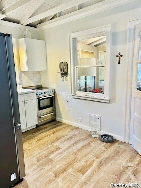 kitchen with tasteful backsplash, stainless steel appliances, white cabinets, vaulted ceiling with beams, and light hardwood / wood-style floors