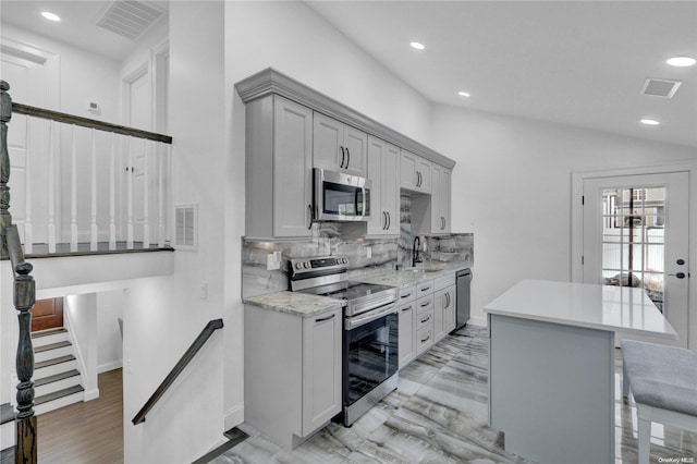 kitchen featuring backsplash, stainless steel appliances, a breakfast bar area, gray cabinets, and lofted ceiling