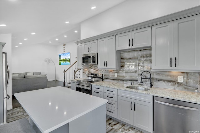 kitchen featuring decorative backsplash, light stone countertops, stainless steel appliances, sink, and light hardwood / wood-style floors