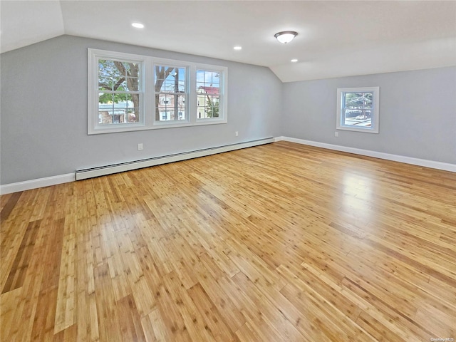 interior space with light wood-type flooring, vaulted ceiling, plenty of natural light, and a baseboard heating unit