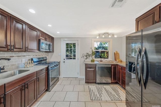 kitchen with sink, tasteful backsplash, crown molding, light tile patterned floors, and appliances with stainless steel finishes