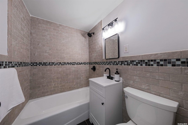 full bathroom featuring tiled shower / bath, vanity, tile walls, and toilet