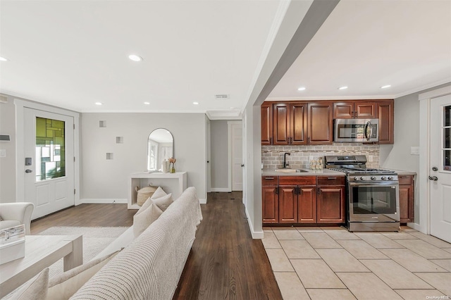 kitchen featuring sink, decorative backsplash, light wood-type flooring, ornamental molding, and appliances with stainless steel finishes