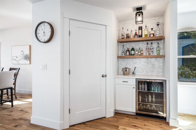 bar with backsplash, wine cooler, white cabinetry, and light hardwood / wood-style floors