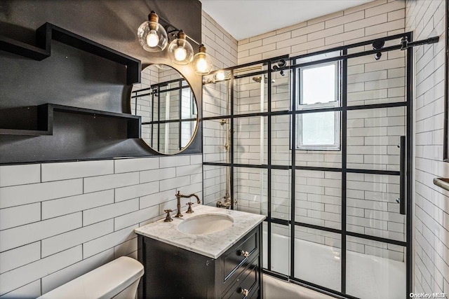 full bathroom featuring combined bath / shower with glass door, toilet, tile walls, and vanity