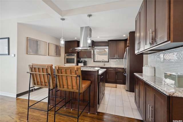 92-52 219th St, Queens Village, NY 11428 - kitchen with appliances with stainless steel finishes, island exhaust hood, decorative backsplash, a center island, and dark brown cabinetry