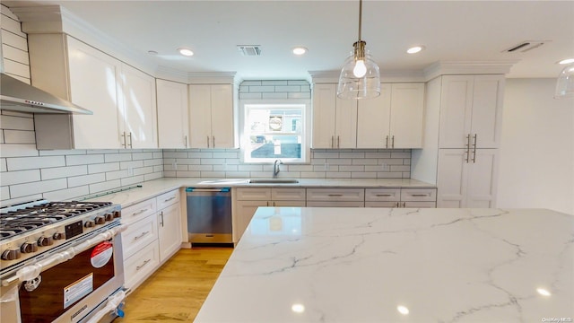 kitchen featuring light stone counters, stainless steel appliances, sink, wall chimney range hood, and light hardwood / wood-style floors