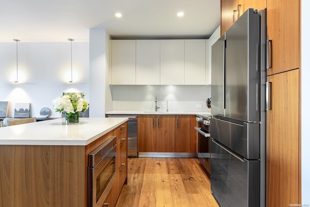 kitchen with stainless steel appliances, sink, pendant lighting, light hardwood / wood-style flooring, and white cabinetry