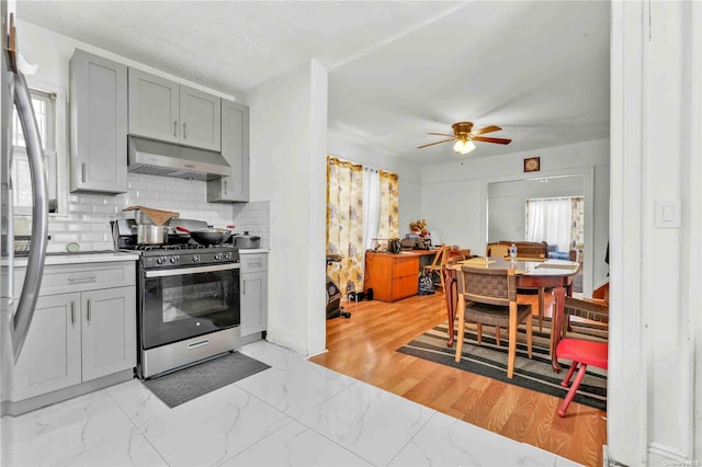 kitchen with ceiling fan, light wood-type flooring, a textured ceiling, appliances with stainless steel finishes, and tasteful backsplash