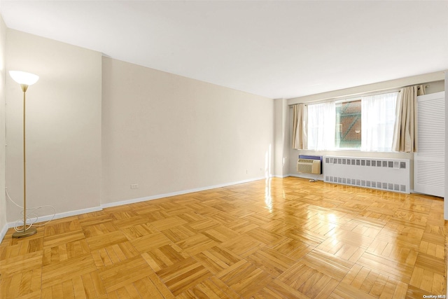 spare room with a wall mounted AC, radiator, and light parquet floors