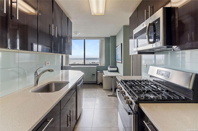 kitchen with sink, light tile patterned floors, a textured ceiling, appliances with stainless steel finishes, and dark brown cabinets