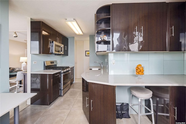 kitchen featuring a breakfast bar, a textured ceiling, stainless steel appliances, sink, and light tile patterned floors