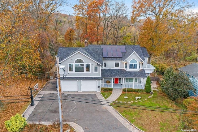 view of front of property featuring covered porch, solar panels, a garage, and a front yard