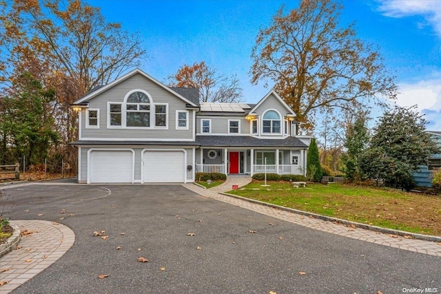 view of front of home featuring covered porch, solar panels, a garage, and a front yard