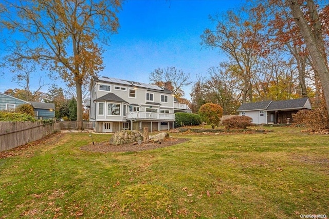 rear view of property featuring a deck, a lawn, and solar panels