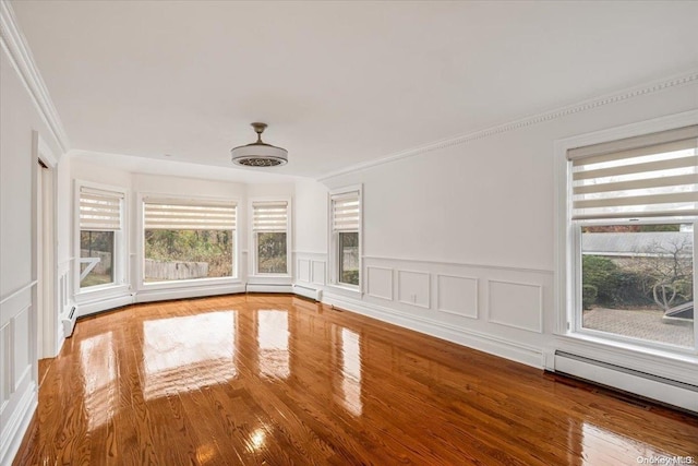 unfurnished room with hardwood / wood-style floors, ornamental molding, baseboard heating, and a wealth of natural light