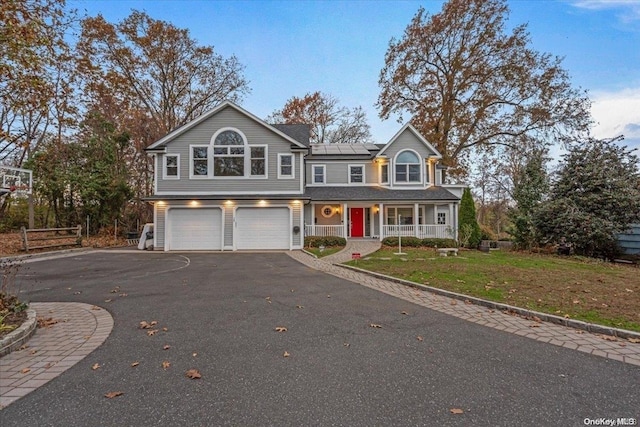 view of property featuring a garage, a front lawn, solar panels, and covered porch