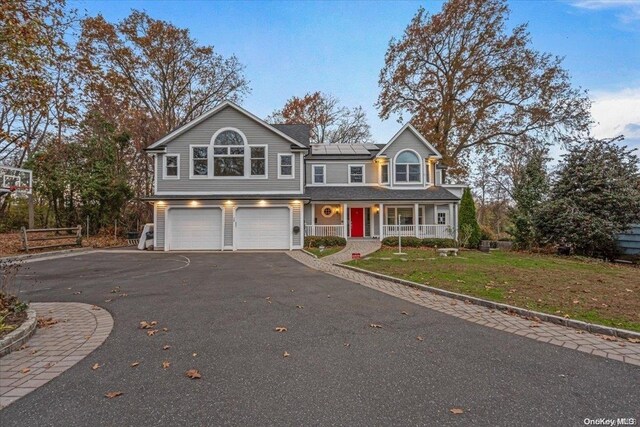 26 Bayville Park Blvd, Bayville, NY 11709 - traditional home featuring covered porch, an attached garage, roof mounted solar panels, driveway, and a front yard
