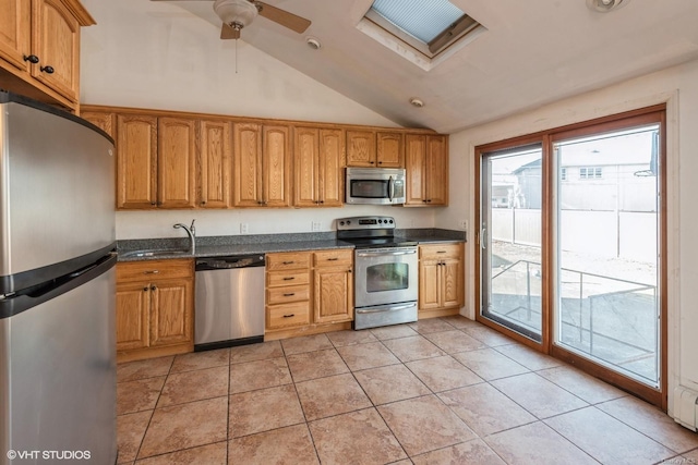 kitchen featuring sink, ceiling fan, stainless steel appliances, vaulted ceiling with skylight, and light tile patterned flooring