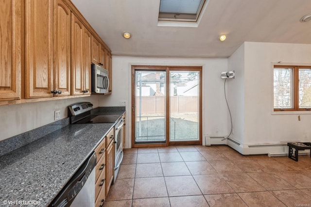 kitchen with a healthy amount of sunlight, stainless steel appliances, light tile patterned floors, and dark stone counters