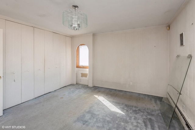 unfurnished bedroom with carpet flooring, baseboard heating, crown molding, an inviting chandelier, and a closet