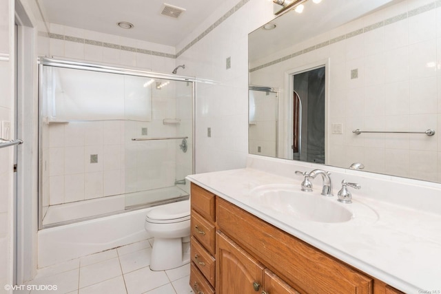 full bathroom with tile patterned floors, toilet, combined bath / shower with glass door, tile walls, and vanity