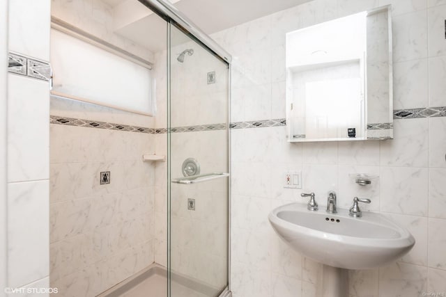 bathroom with a shower with shower door, sink, and tile walls