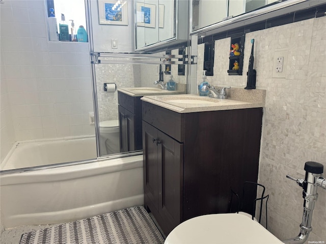 full bathroom featuring vanity, toilet, shower / bath combination with glass door, and tile walls