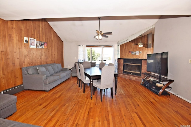 dining area featuring lofted ceiling, wooden walls, ceiling fan, wood-type flooring, and a tiled fireplace