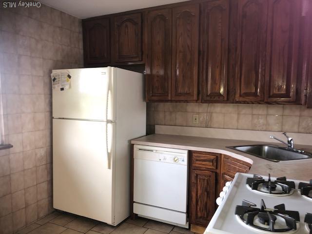 69 E 1st St, Freeport, NY 11520 - kitchen featuring white appliances, a sink, tile walls, light tile patterned floors, and light countertops