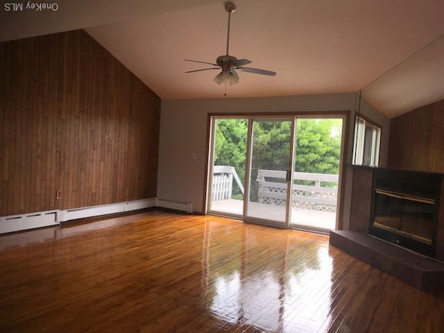 69 E 1st St, Freeport, NY 11520 - unfurnished living room featuring wood walls, vaulted ceiling, ceiling fan, wood finished floors, and a glass covered fireplace