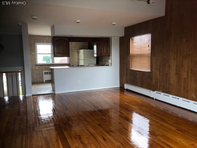 69 E 1st St, Freeport, NY 11520 - unfurnished living room with radiator heating unit, wood finished floors, a baseboard heating unit, and wood walls