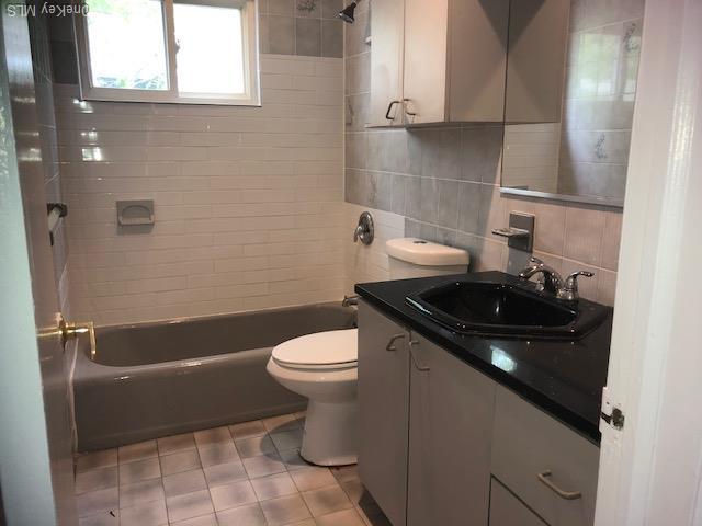 69 E 1st St, Freeport, NY 11520 - bathroom with vanity, toilet, washtub / shower combination, tile patterned floors, and tasteful backsplash