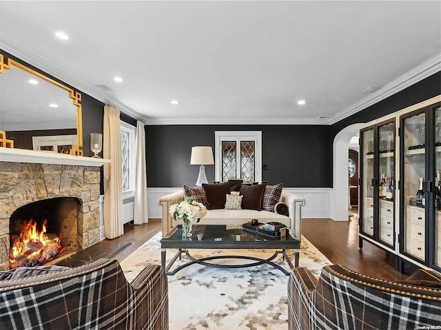 living room with a stone fireplace, wood-type flooring, and ornamental molding