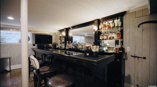 bar featuring a healthy amount of sunlight, dark hardwood / wood-style flooring, and wooden walls