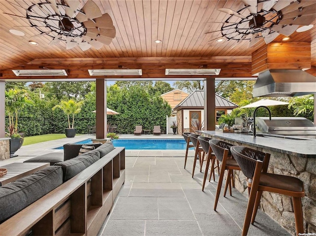 view of swimming pool featuring an outdoor hangout area, exterior bar, ceiling fan, a grill, and exterior kitchen