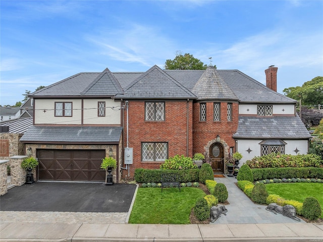 38 Royal Ct, Rockville Centre, NY 11570 - view of front facade featuring a high end roof, asphalt driveway, a front yard, brick siding, and a chimney