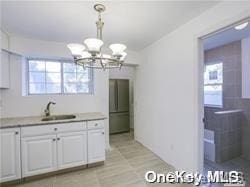 kitchen featuring stainless steel fridge, sink, pendant lighting, a chandelier, and white cabinetry