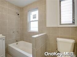 full bathroom with toilet, vanity, tile walls, and tiled shower / bath