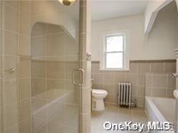 bathroom featuring shower with separate bathtub, toilet, radiator heating unit, and tile walls