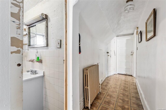 corridor featuring radiator, tile walls, and a textured ceiling