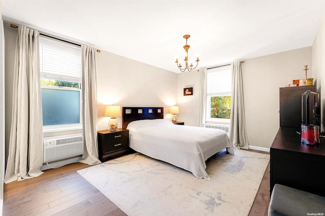 bedroom with multiple windows, a wall mounted AC, a chandelier, and hardwood / wood-style flooring