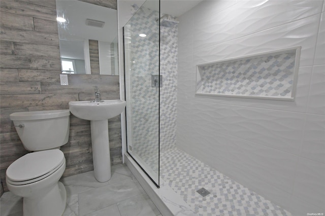 bathroom with a tile shower, toilet, and tile walls