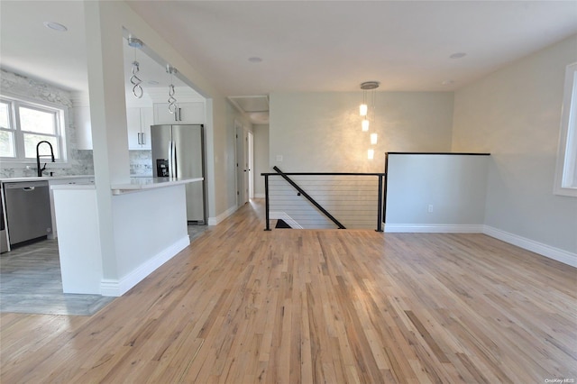 kitchen featuring appliances with stainless steel finishes, light wood-type flooring, sink, pendant lighting, and white cabinets