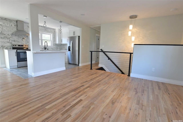 interior space with stainless steel appliances, hanging light fixtures, light hardwood / wood-style floors, and wall chimney range hood