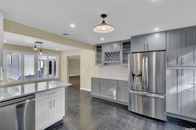 kitchen with gray cabinetry, dark wood-type flooring, decorative backsplash, decorative light fixtures, and stainless steel appliances