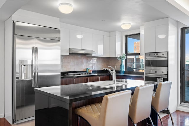 kitchen featuring a kitchen bar, appliances with stainless steel finishes, a kitchen island with sink, sink, and white cabinetry